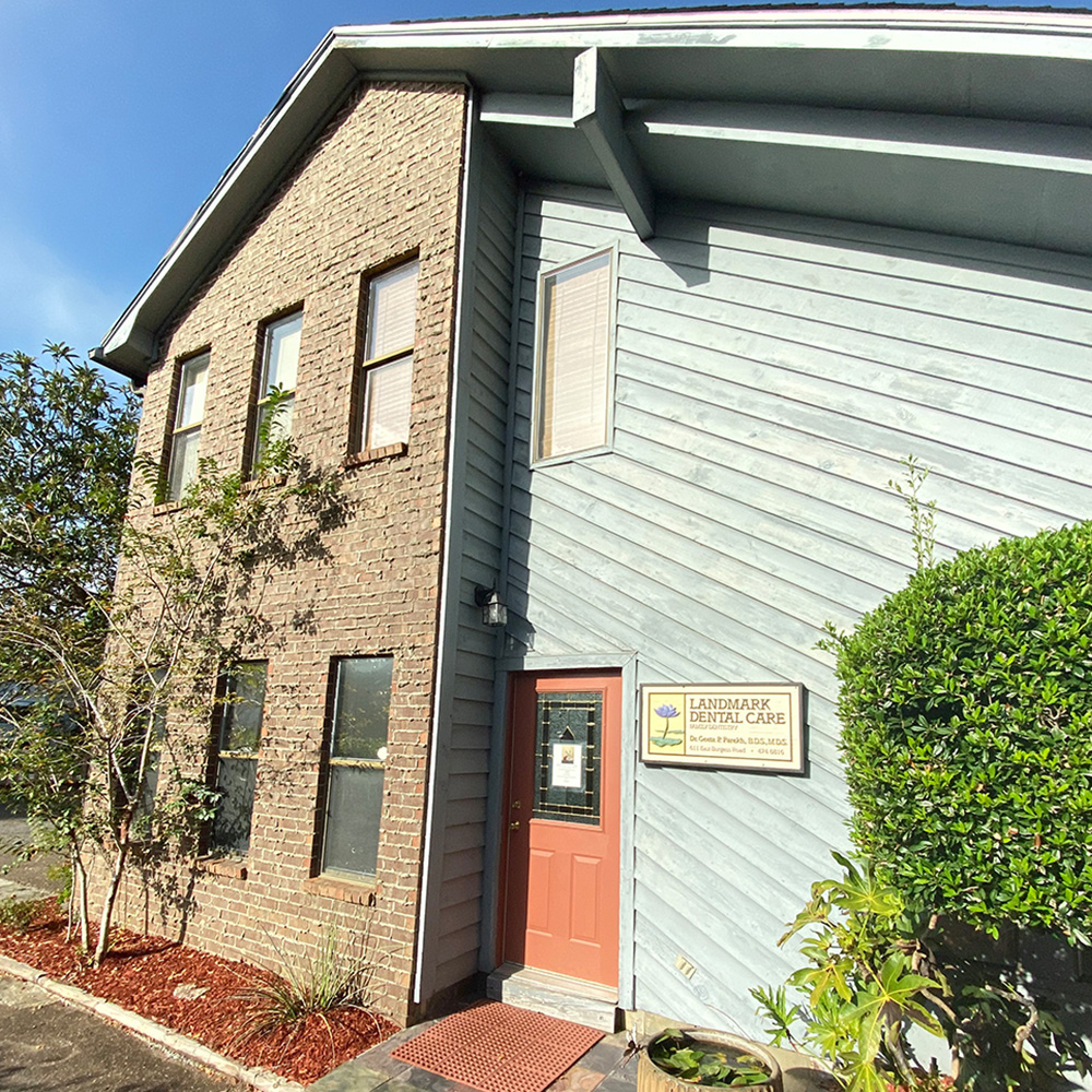 The image shows a two-story building with a prominent sign that reads Lighthouse Christian Church. It has a brick facade and is topped by a white roof. The entrance features a red door and a small porch area. In front of the building, there are plants and a sidewalk leading up to the entrance.