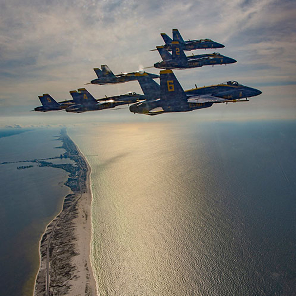 Four blue and yellow fighter jets flying in formation over a vast expanse of ocean.